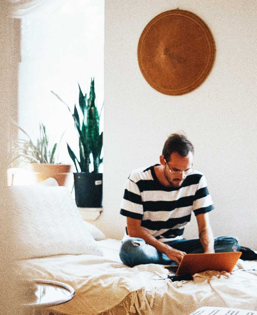 Hombre sentado en la cama trabajando con un portátil